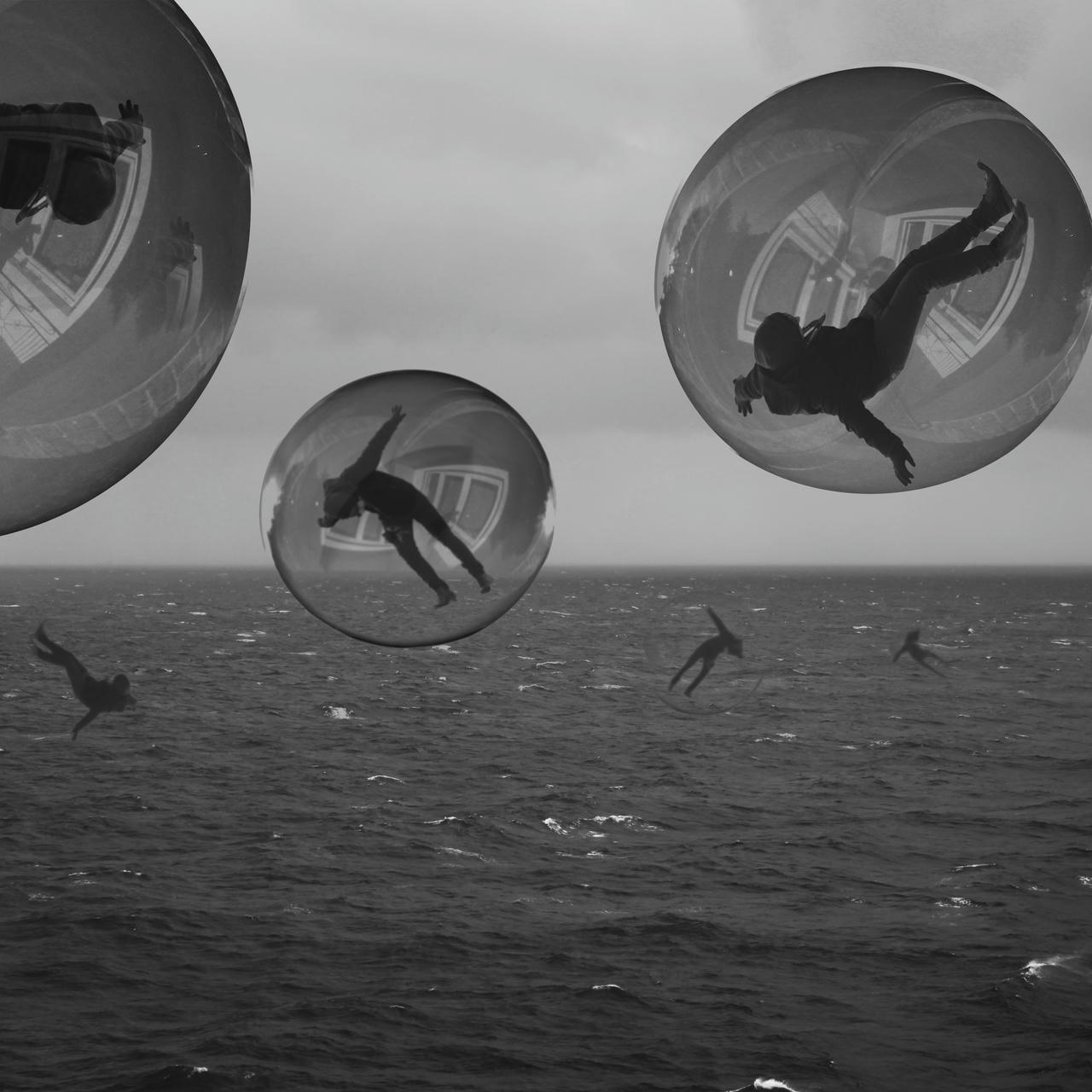 Black and white picture in the middle of an agitated sea. There is nothing but clouds on the horizon and an overcast sky. In the front, silhouettes of men floating in reflective bubbles.